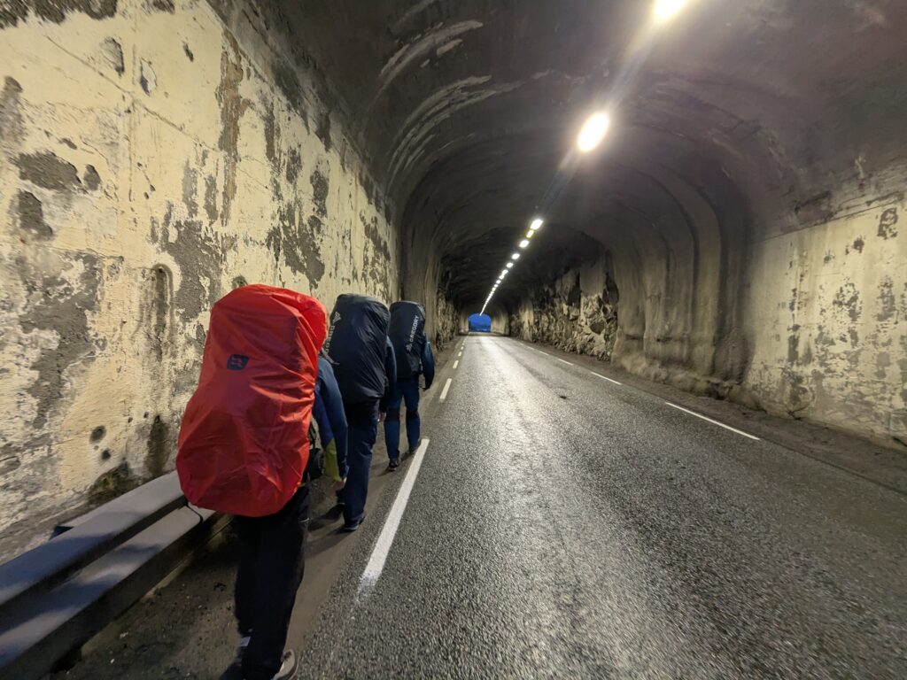 three persons with big backpacks walking in the tunnel, on the way from the airport to Svolvær 