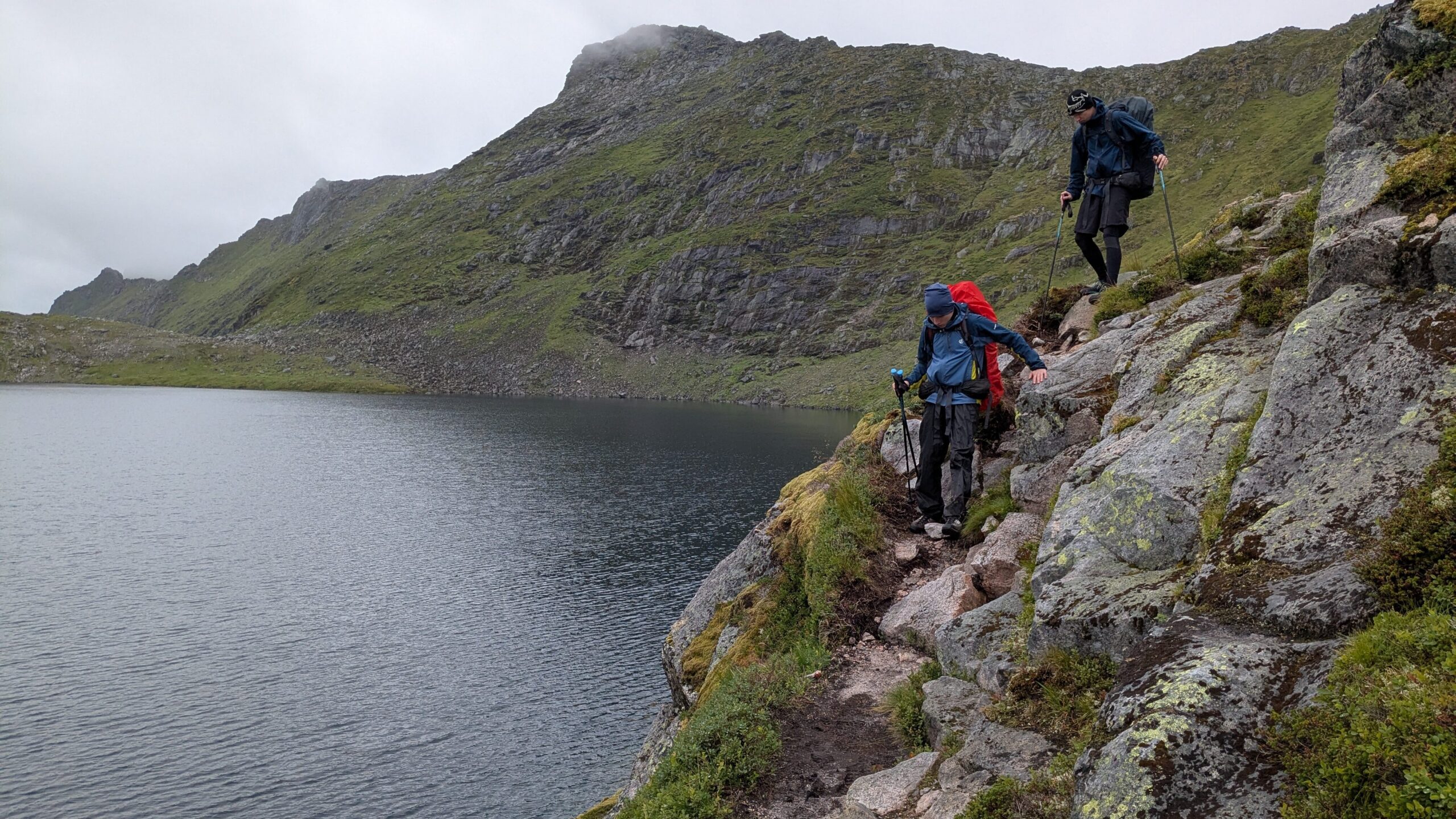 Hikers with backpacks descending toward Bosvatnet Lake on the Long Lofoten Trail, Lofoten Islands, Norway.