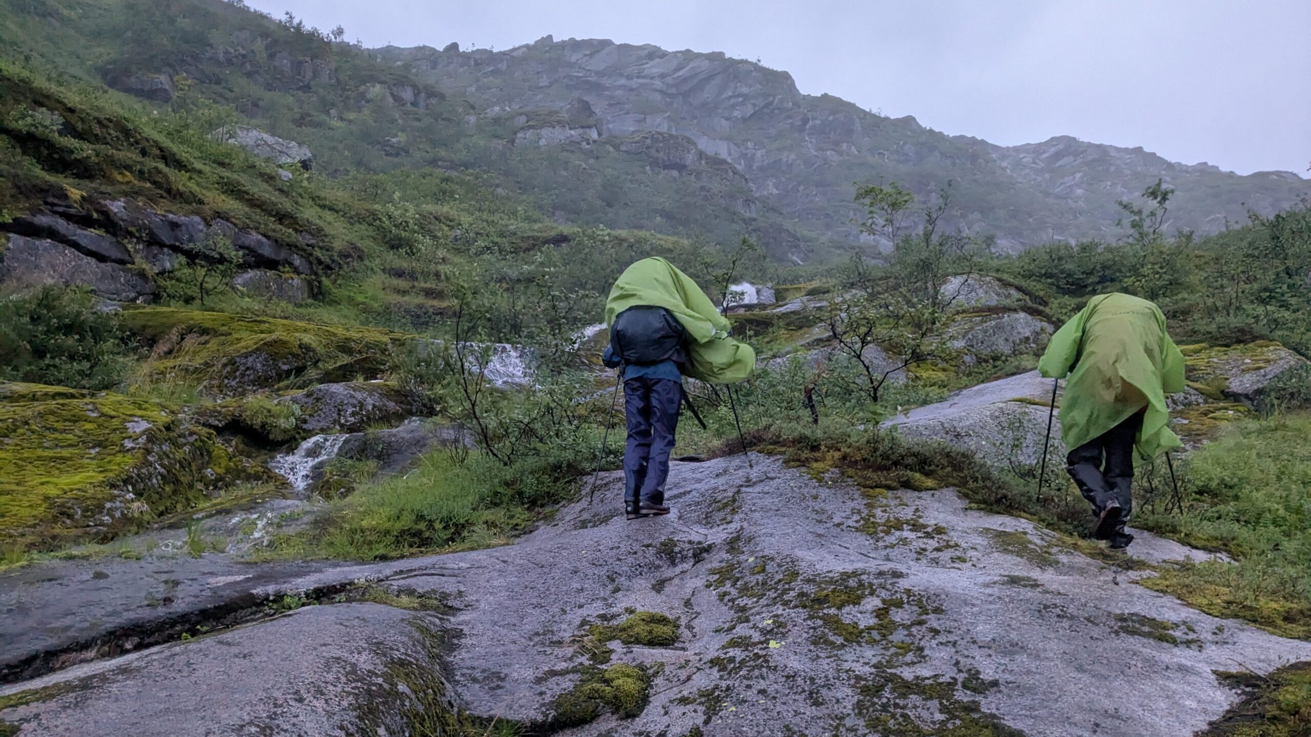 Hikers trekking through wind and rain near Nokkvatnet on the Long Lofoten Trail.