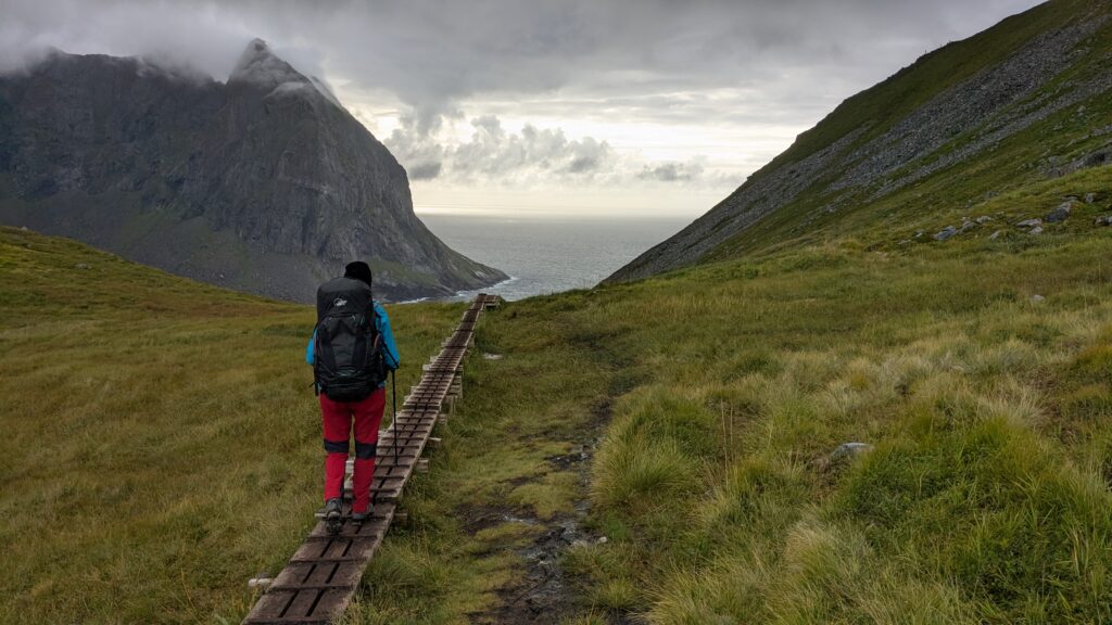 Backpacker hiking along boardwalks on the trail to Kvalvika Beach, Lofoten Islands