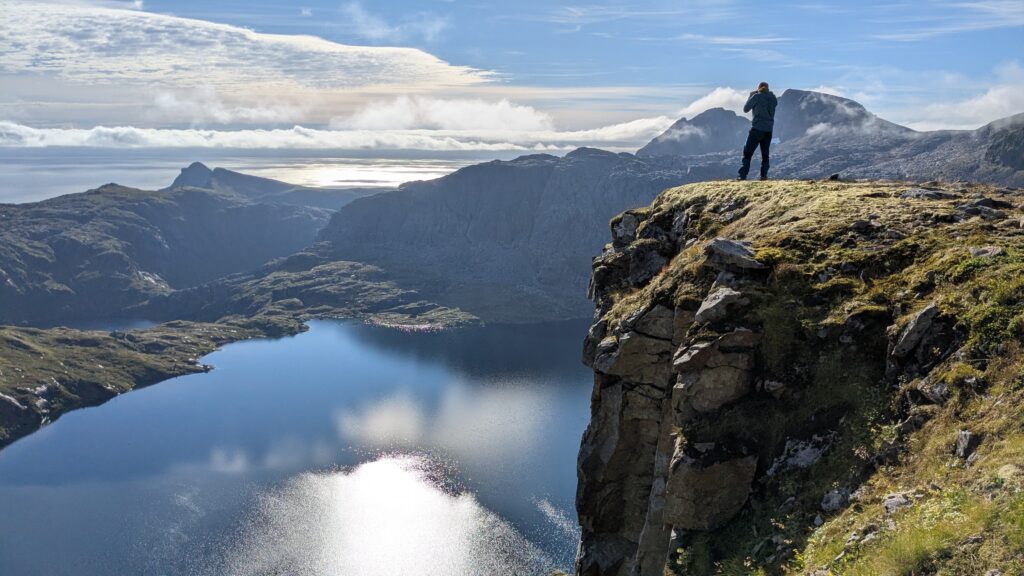 hiker with backpack overlooking fjord valley, on the cliff