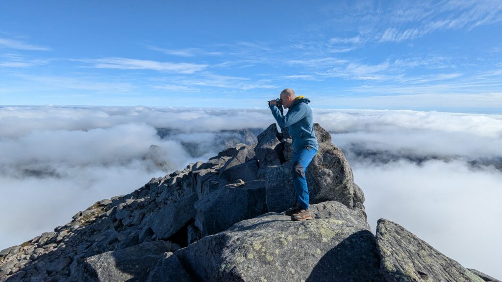 hiker sitting on rocky summit above clouds, Hermannsdalstinden, Lofoten, Norway