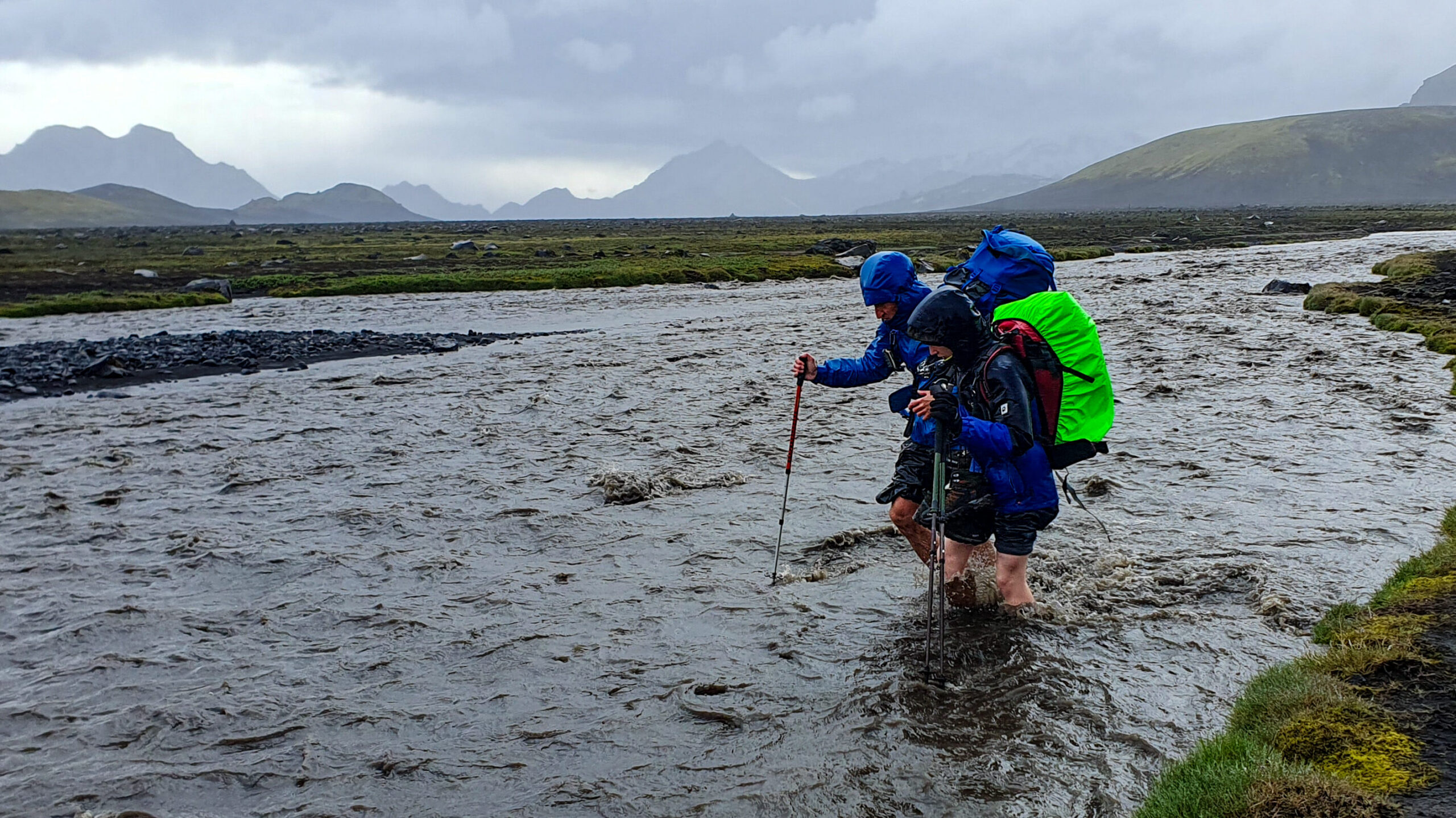 two persons with heavy backpacks crossing glacial river in heavy rain, Laugavegur Trail, Icelan