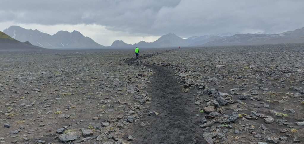 Hiker crossing a rocky volcanic plain between Hvanngil and Emstrur on the Laugavegur Trail, Iceland.