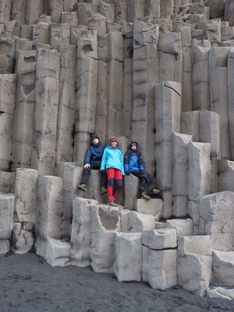 Three persons standing among the basalt columns at Reynisfjara Black Sand Beach, Iceland.