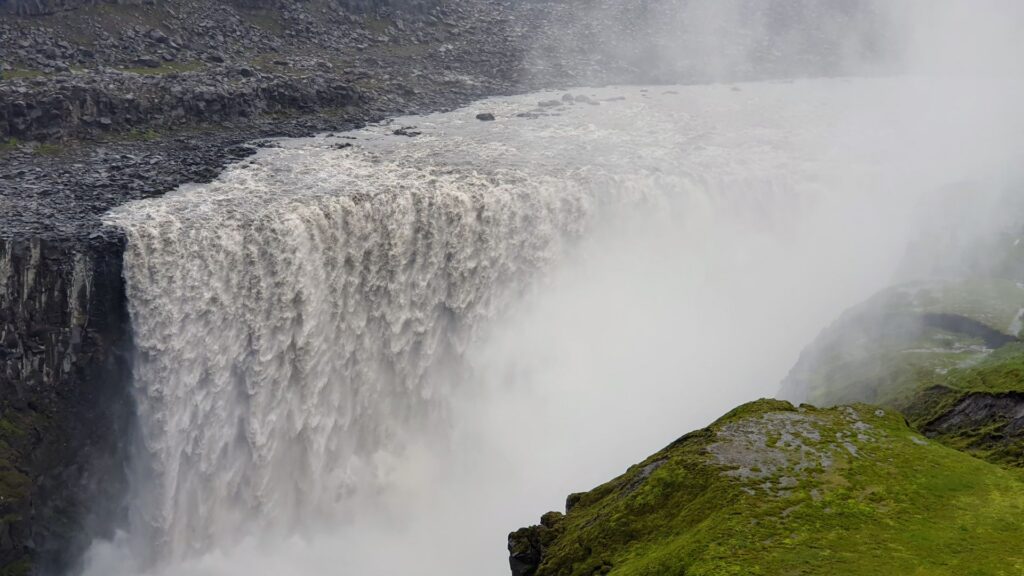 Powerful Dettifoss waterfall seen from the east bank with heavy spray rising above the canyon.