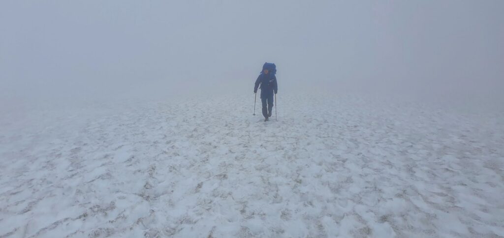 Lone hiker crossing a snowfield in dense fog near Hrafntinnusker on the Laugavegur Trail.