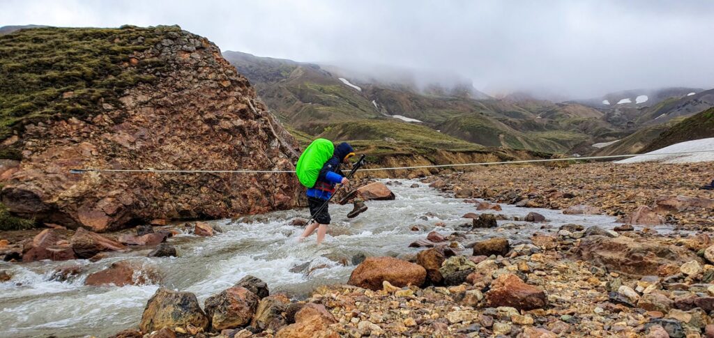 Hiker crossing a glacial river on the way to Álftavatn on the Laugavegur Trail, Iceland.