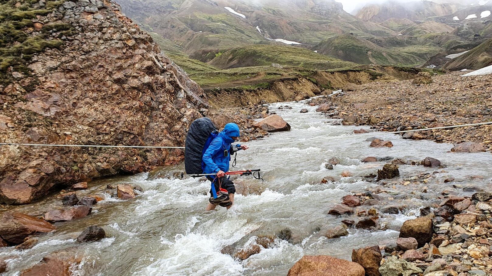 backpacker crossing the cold river in rain, Laugavegur Trail, Icela